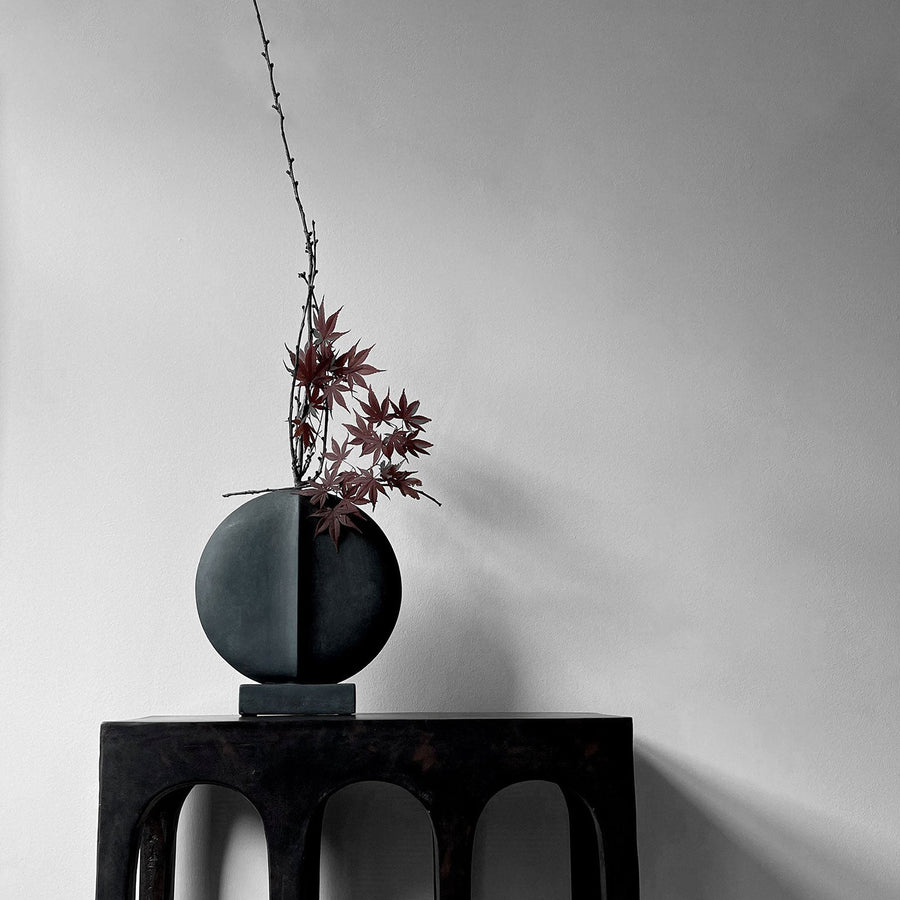 The 101Cph Guggenheim Mini Black 111126 vase by 101 Copenhagen sits on a wooden table in an interior setting.