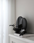 A 101Cph Guggenheim Mini Black 111126 vase sits on a mantle in an interior setting. (Brand Name: 101 Copenhagen)