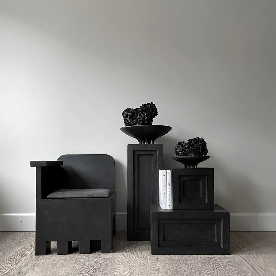 A black chair sits on a wooden floor, accompanied by a 101Cph Medusa Tray Mini Coffee 221064 from the brand 101 Copenhagen.
