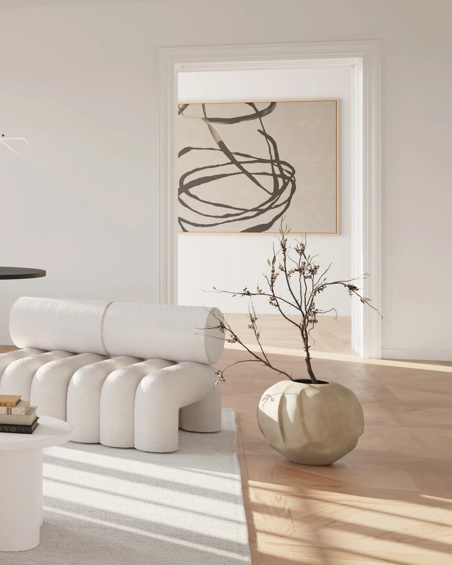 Modern interior with white furniture, a vase with branches, and abstract art on a light-colored wall.