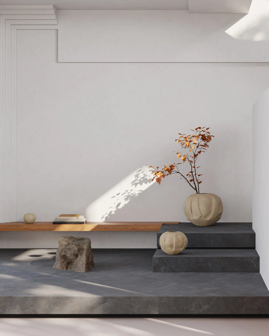 Modern interior with a white wall, wooden bench, stone stools, and decorative items.