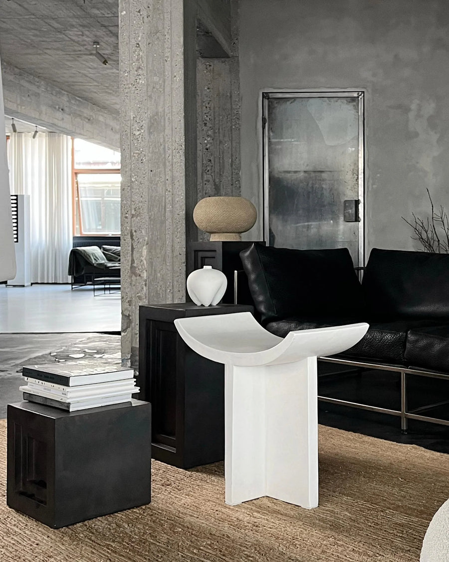 Modern interior with a black sofa, white table, and concrete walls.