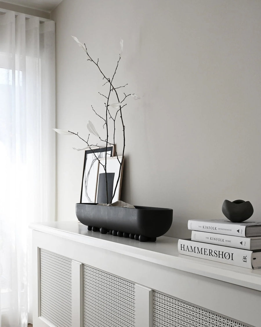 Decorative setup with black bowl, branches, and books on a white surface.