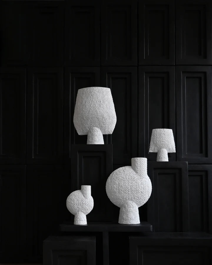 A group of unique and sculptural 101Cph Sphere Square Shisen Big Bone White 231011 vases with a detailed finish on a black table. Brand: 101 Copenhagen.