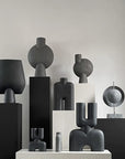 A group of 101 Copenhagen Bubl Big Dark Grey 201015 vases in a dark grey finish on a white pedestal.
