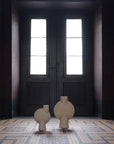 Two 101Copenhagen Sphere Vase Bubl Big Sand 201014 vases from 101 Copenhagen are elegantly placed on a tile floor in an empty room.