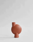 A small red 101Cph Sphere Vase Bubl Medio Cinnamon 221035 (Limited Edition) by 101 Copenhagen, with a cinnamon finish, sitting on a white surface.