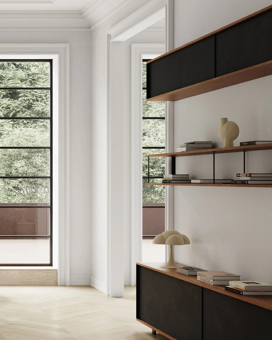 Modern interior with a shelf, lamp, and books in a room with large windows.