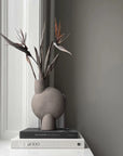 Gray vase with dried plants on books against a gray wall from 101 Copenhagen at Spacio retail stores in Mumbai & Kolkata. 