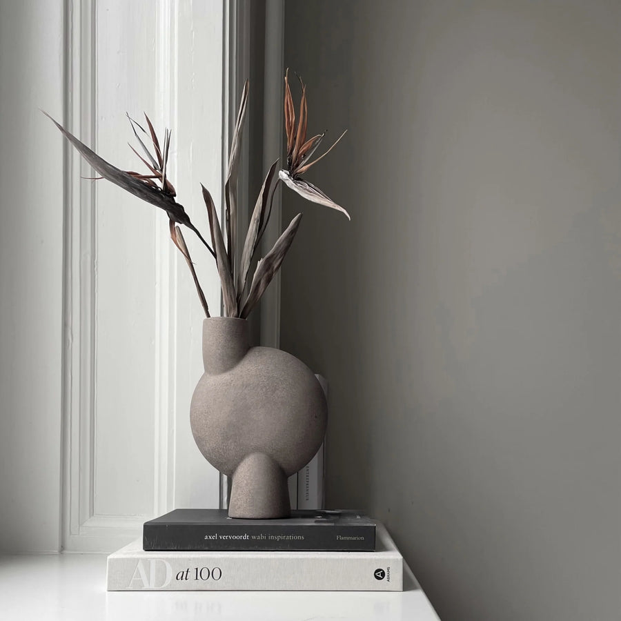 Gray vase with dried plants on books against a gray wall from 101 Copenhagen at Spacio retail stores in Mumbai & Kolkata. 