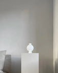 A 101Cph Sphere Vase Bubl Mini Bubble White 202003 from the 101 Copenhagen brand sits next to a grey couch in a room.