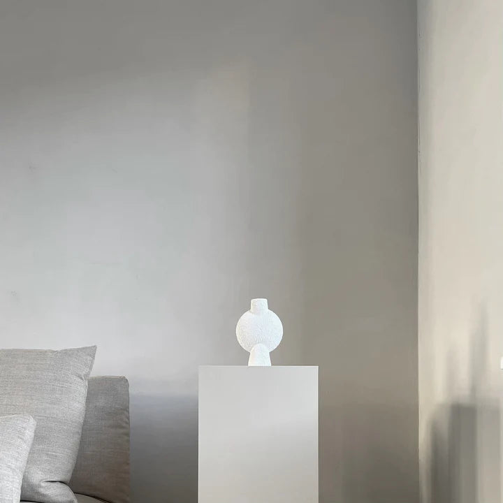 A 101Cph Sphere Vase Bubl Mini Bubble White 202003 from the 101 Copenhagen brand sits next to a grey couch in a room.