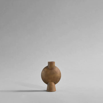 A small wooden vase with an ochre finish, displayed on a grey background. Made by the Scandinavian brand 101 Copenhagen, this vase is known as the 101Cph Sphere Vase Bubl Mini Ocher 111180.