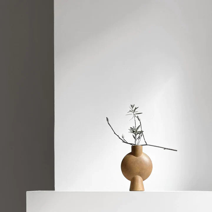 A 101Cph Sphere Vase Bubl Mini Ocher 111180 by 101 Copenhagen sits on top of a white wall.