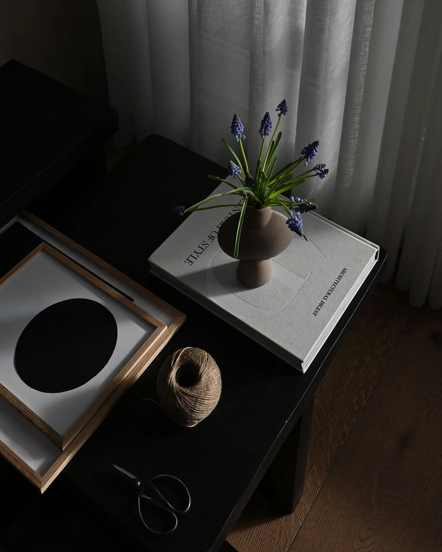 Vase with flowers on a book on a dark surface with a curtain in the background