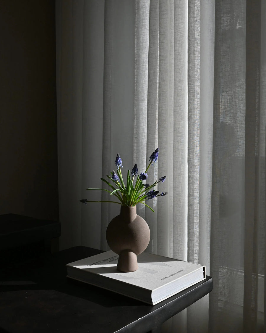 Sculptural Vase with flowers on a book against a curtain backdrop from 101 Copenhagen at Spacio retail stores in Mumbai & Kolkata. 