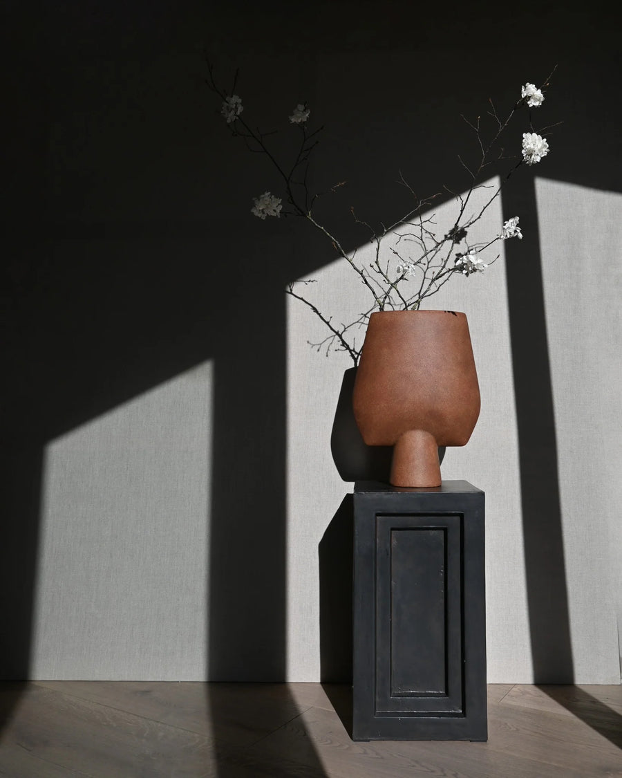 A brown 101 Copenhagen 101Cph Sphere Vase Square Big Terracotta 212008 with a Terracotta finish sits on a table in front of a window.