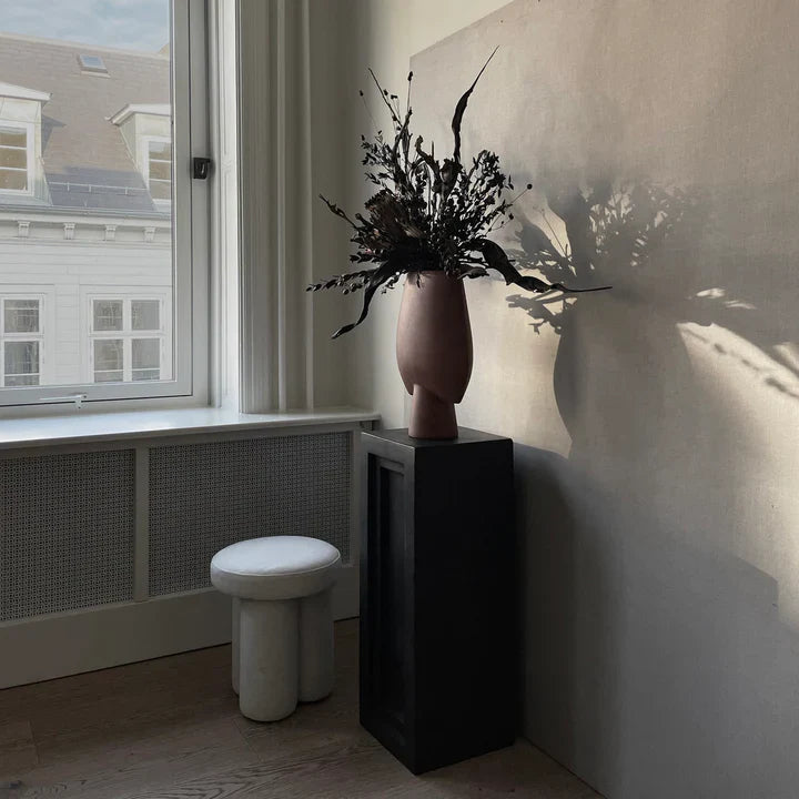 A 101Cph Sphere Vase Square Big Terracotta 212008 from the 101 Copenhagen brand sits on a table in front of a window.