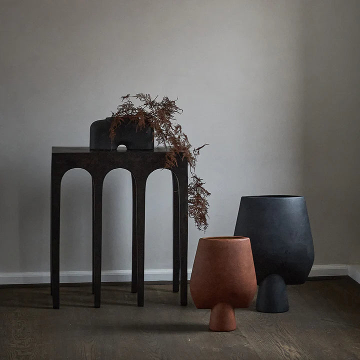 Three 101 Copenhagen Sphere Vase Square Big Terracotta 212008, with a terracotta finish, placed on a wooden table in a room.