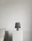 A Scandinavian brand 101 Copenhagen Sphere Vase Square Mini Dark Grey 111020 from the Sphere collection sits on a pedestal in a living room.