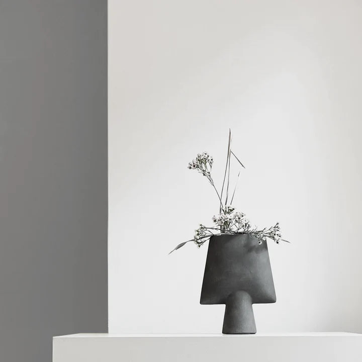 A black 101 Copenhagen Sphere Vase Square Mini Dark Grey 111020 sitting on a table next to a white wall.