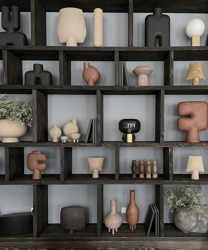 A shelf full of various vases and pots, including a 101 Copenhagen Sphere Vase Square Mini Ocher 111181 with an ochre finish.