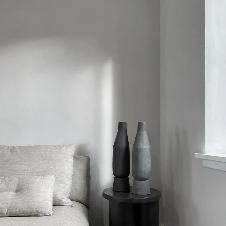 A grey and white Scandinavian bedroom with a bed, a coffee finish table, and a 101Cph Sphere Vase Tall Coffee 111205 by 101 Copenhagen as decoration.