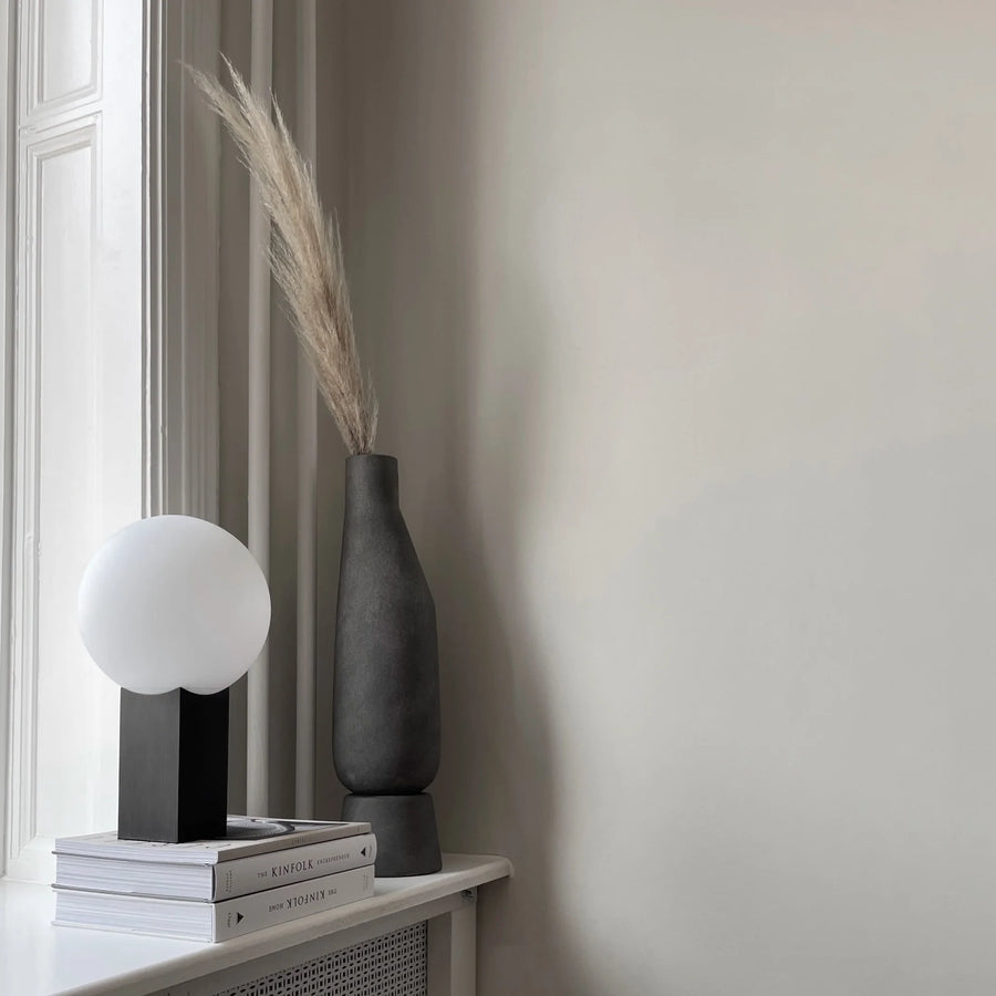 A 101 Copenhagen table lamp with a dark grey finish sits on a window sill next to a book, creating a perfect blend of Scandinavian living style.