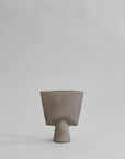 A taupe color 101 Copenhagen vase in a triangle shape with a grey back ground. Available at Spacio India