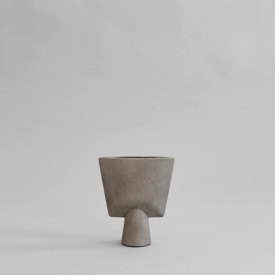 A taupe color 101 Copenhagen vase in a triangle shape with a grey back ground. Available at Spacio India