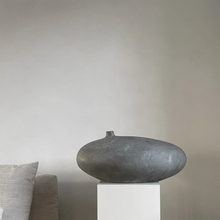 Decorative vase on a pedestal against a plain wall with a pillow partially visible  from 101 Copenhagen at Spacio retail stores in Mumbai & Kolkata. 