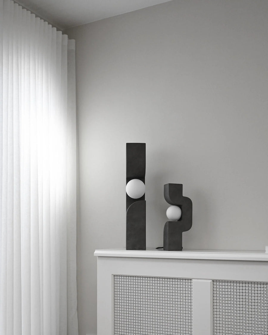 Two black abstract sculptures on a white surface against a gray wall from 101 Copenhagen at Spacio retail stores in Mumbai & Kolkata. 