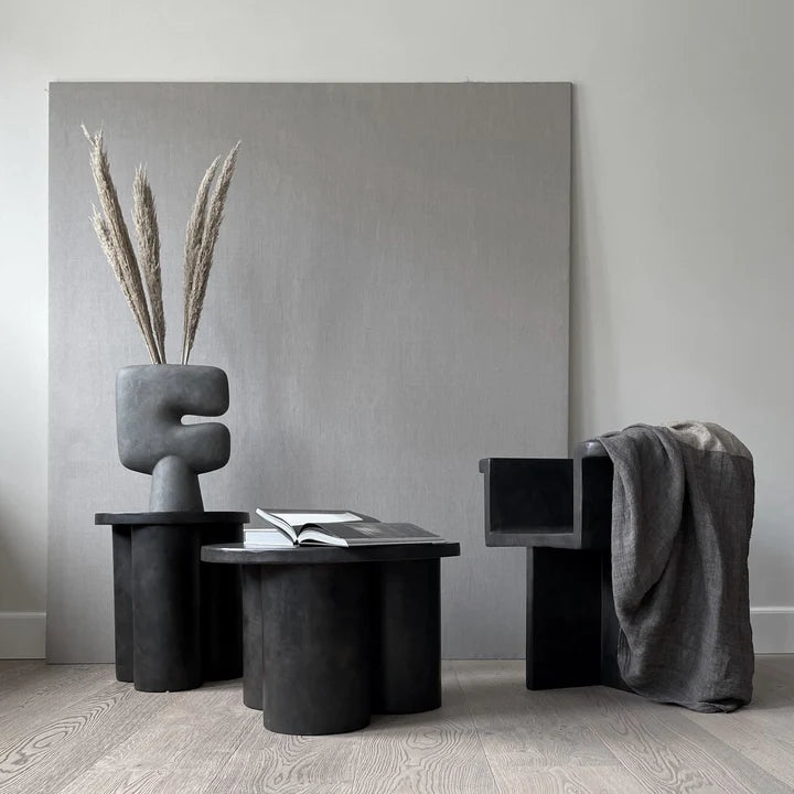 A modern ceramic vase with a tribal-inspired design in a rich dark grey finish by 101CPH in a room setting with foliage. Available at Spacio India