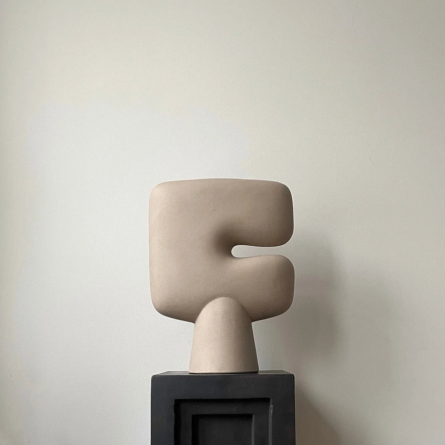 Beige abstract sculptural vase on a black base against a plain background from 101 Copenhagen at Spacio retail stores in Mumbai & Kolkata. 