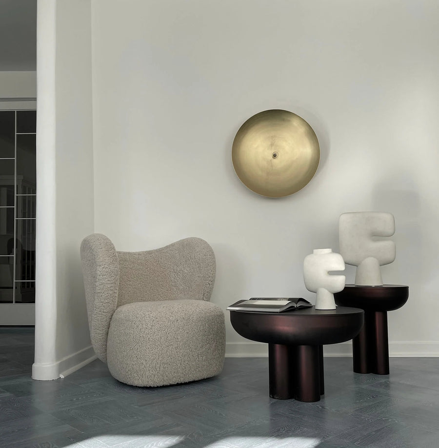 Modern interior with a textured armchair, round table, and abstract sculpture against a white wall.