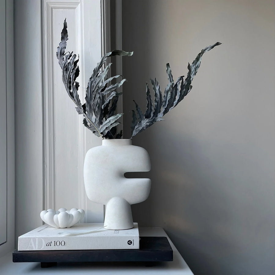White vase with dried plants on a shelf styled with coffee table books against a gray wall from 101 Copenhagen at Spacio retail stores in Mumbai & Kolkata. 