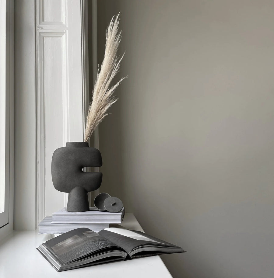 A 101Cph Tribal Vase Medio Dark Grey 214003 by 101 Copenhagen and a Dark Grey Colour book on a window sill.  Available at Spacio India