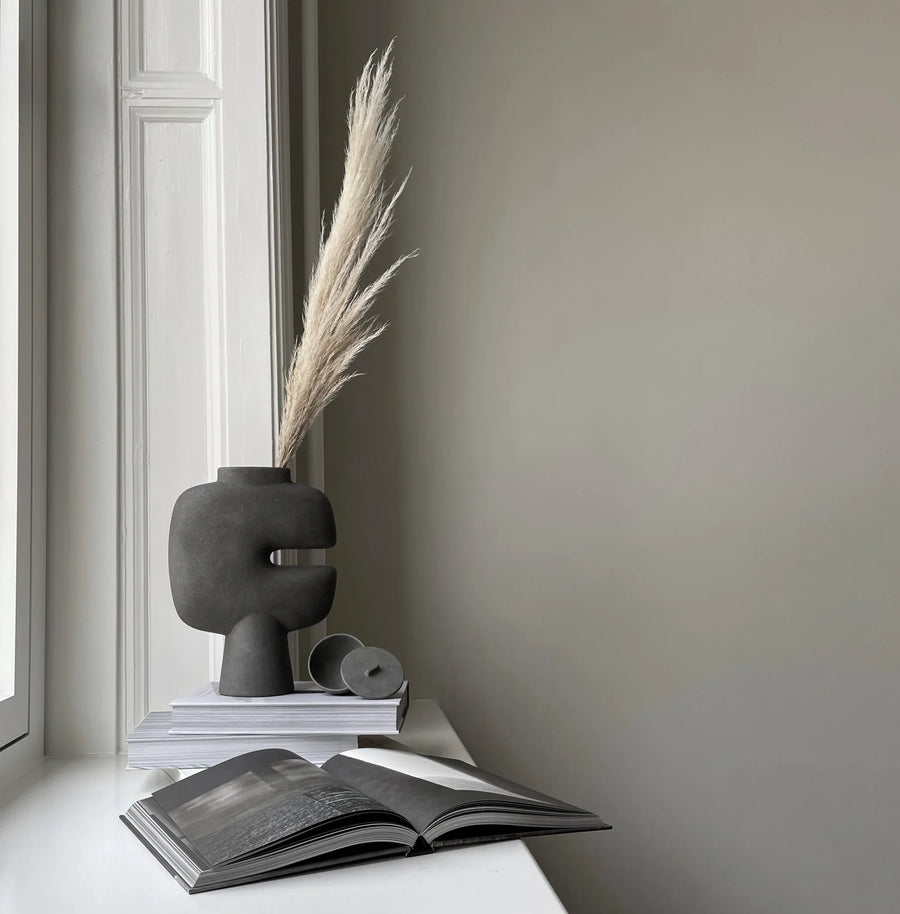 A 101Cph Tribal Vase Medio Dark Grey 214003 by 101 Copenhagen and a Dark Grey Colour book on a window sill. Available at Spacio India