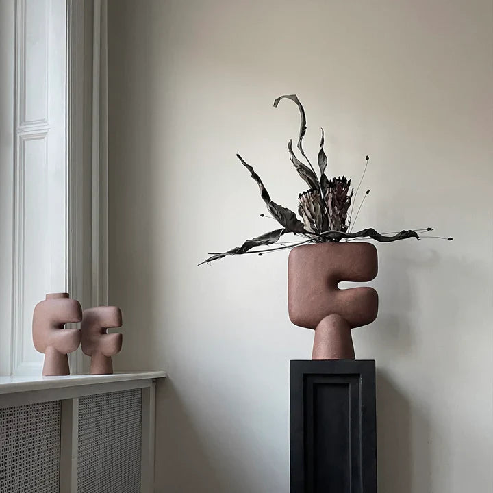 Two sculptures from the Tribal Collection, displayed on a table in front of a window. The sculptures, including the 101Cph Tribal Vase Medio Terracotta 214004, showcase stunning terracotta colors. The sculptures, including the 101Cph Tribal Vase Medio Terracotta 214004, showcase stunning terracotta colors.