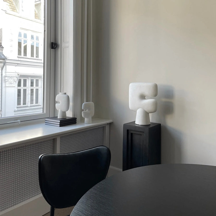 Modern interior with white sculptures on a windowsill and pedestal (plinth) black chair.
