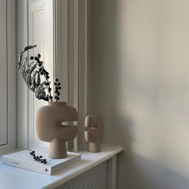 Two 101Cph Tribal Vase Mini Sand 221002s sit on a window sill next to a book from the Tribal Collection. Available at Spacio India