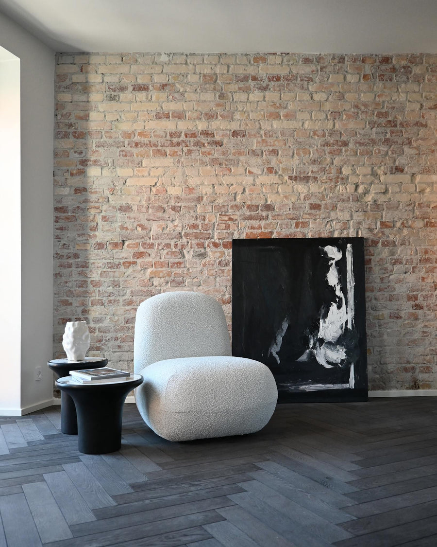 Modern living room with a textured brick wall, white armchair, and abstract painting.