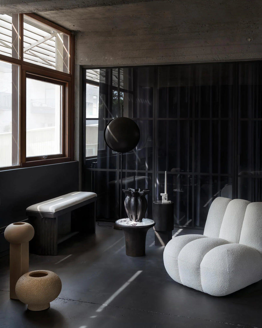 Modern interior with a white armchair, black bench, and decorative vases.