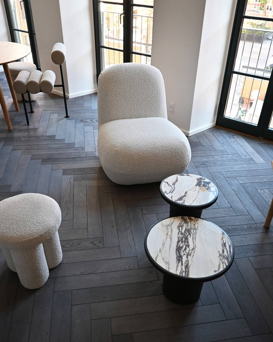 Modern interior with textured chairs and marble tables on a wooden floor.