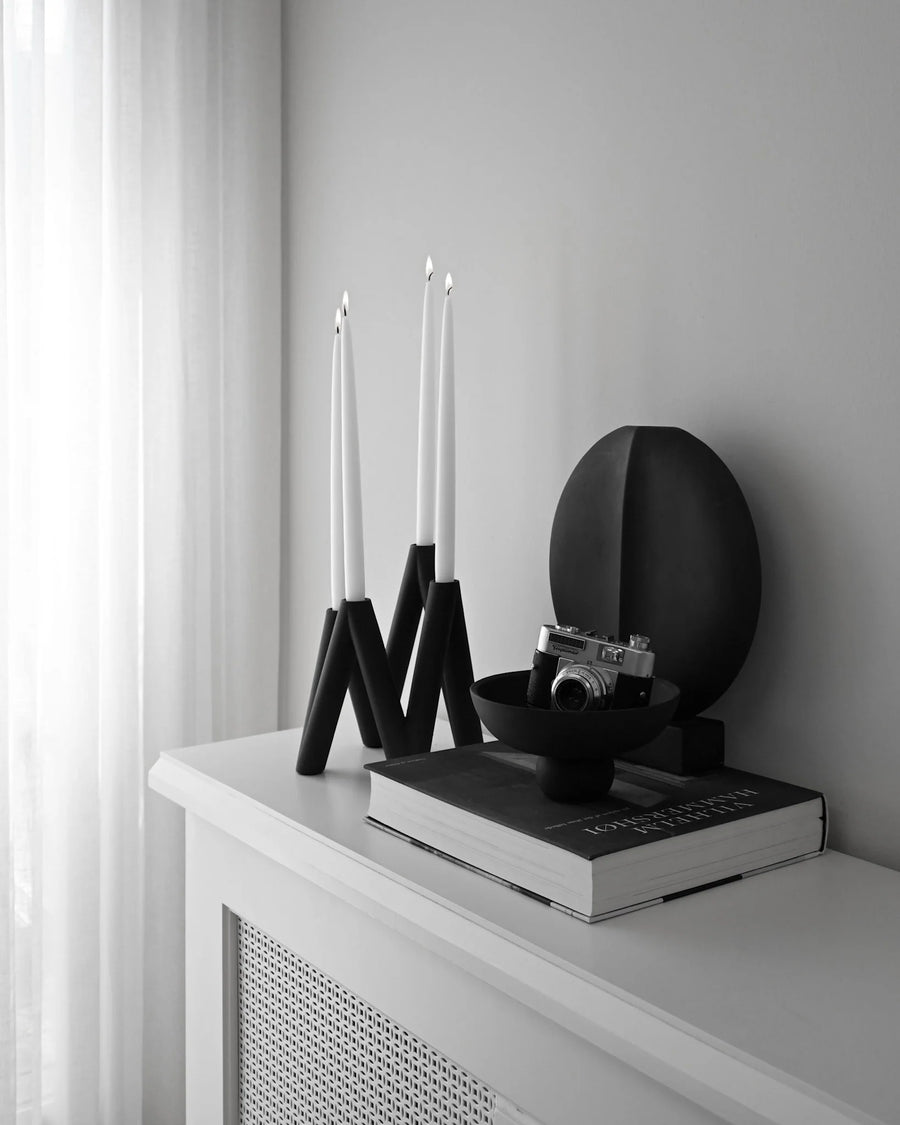 Decorative setup with black vases, candles, and a book on a white surface.