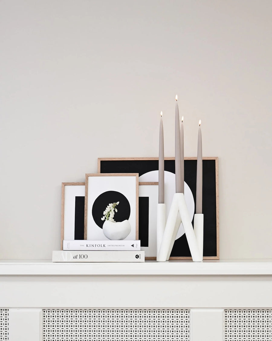 Decorative shelf with framed art, candles, and books against a plain wall.