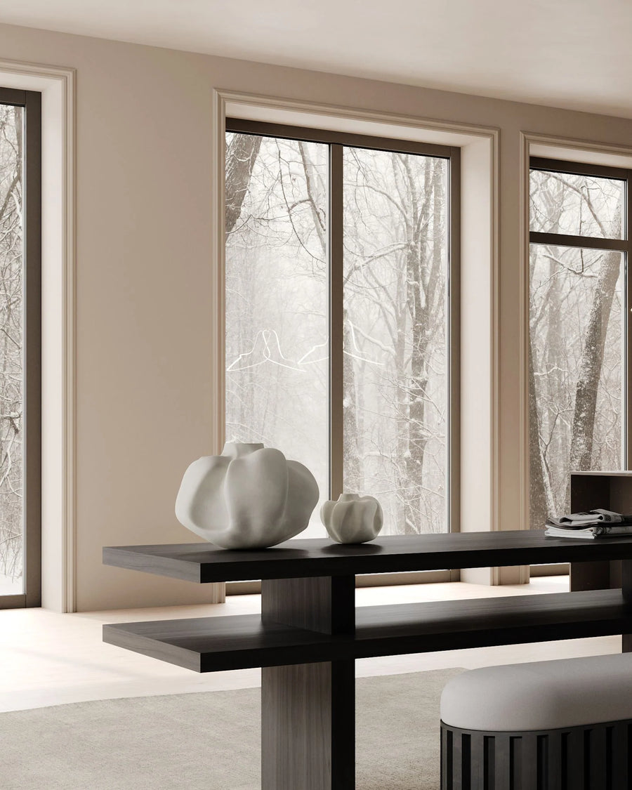 Modern interior with a black dining table and white chairs, large windows showing trees outside.