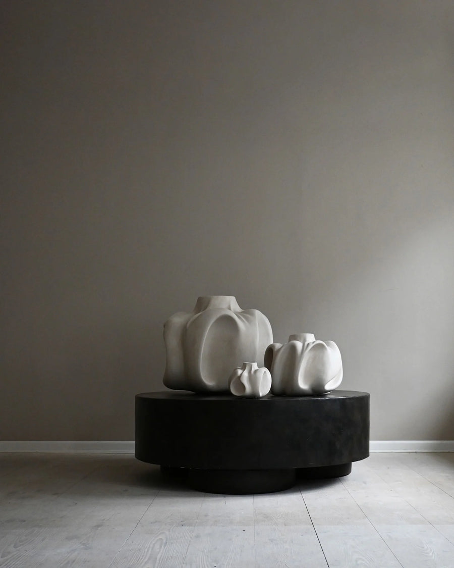 Three white ceramic sculptures on a black round platform against a plain wall from 101 Copenhagen at Spacio retail stores in Mumbai & Kolkata. 