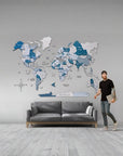 Man standing next to a world map wall decoration in a room with a gray sofa.