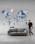Man standing next to a large world map on a wall in a modern living room.